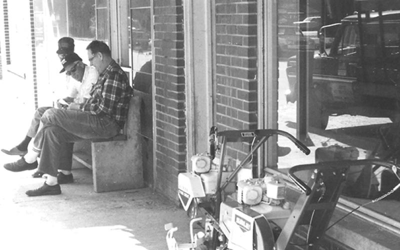 For many years Charles Freel would sit on the bench outside his furniture store on Main Street and visit with the locals who stopped by. It was like a scene in a Norman Rockwell painting. Sitting beside him is Jack Ledford, but the writer could not identify the next man. You can tell it was a nice spring day, as the garden tillers were displayed on the sidewalk. 